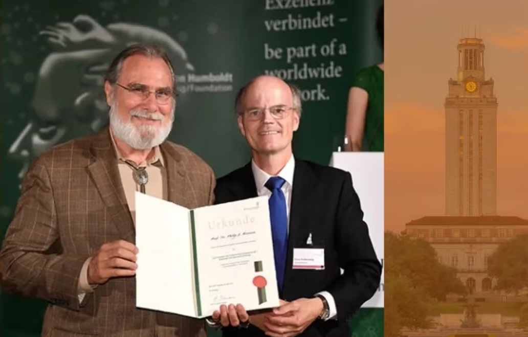 A man with a beard is presented with a certificate in front of a sign in German.